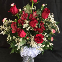 Red roses and red alstroemeria in a clear vase with white ribbon