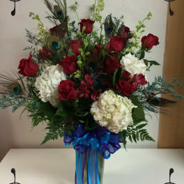 Red roses and white hydrangeas in a tall vase with peacock feathers