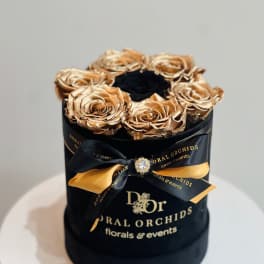 Gold roses in a black round box with a ribbon bow