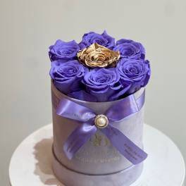 Purple roses in a round lavender box with a gold rose center and ribbon bow