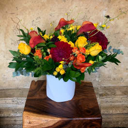 Colorful floral arrangement in a white vase with yellow, orange, and burgundy blooms