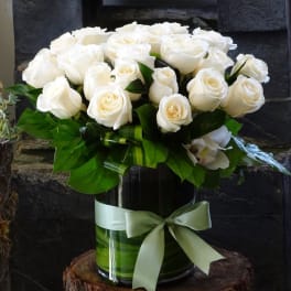 White roses arranged in a glass vase with a pale green ribbon