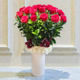Red roses arranged in a white vase with white and burgundy flowers