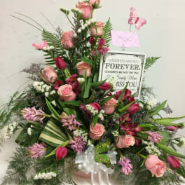 Pink roses and mixed blooms in a sympathy arrangement with a memorial sign