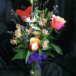 Mixed bouquet of roses and white flowers in a glass vase with a purple ribbon