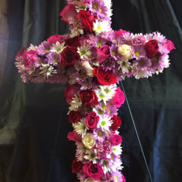 Cross-shaped floral arrangement with roses and daisies on a dark stand