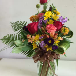 Mixed bouquet of roses, daisies, and purple flowers in a glass vase