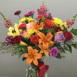 Mixed bouquet of lilies, roses, and chrysanthemums in a glass vase with a red ribbon