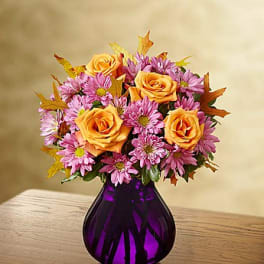 Orange roses and pink daisies in a purple glass vase