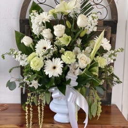 White floral arrangement in a pale blue vase with a white ribbon