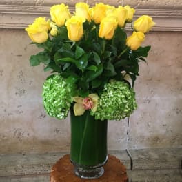 Yellow roses and green hydrangeas in a tall glass vase