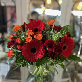 Bouquet of red gerbera daisies and orange roses in a glass vase