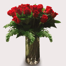 Red roses arranged in a clear glass vase with fern accents