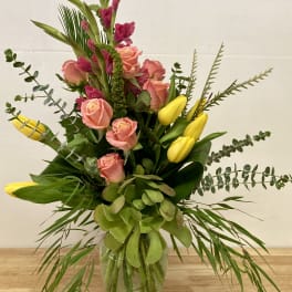 Pink roses and yellow tulips in a glass vase with greenery