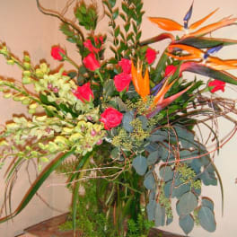 Tall tropical arrangement with orange bird-of-paradise and pink roses in a glass vase