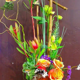 Tall tropical floral arrangement in an orange vase with orchids and roses