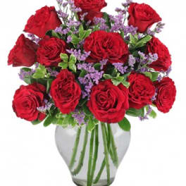 Red roses and purple filler flowers arranged in a clear glass vase