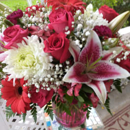 Mixed bouquet of pink roses, lilies, and white chrysanthemums in a glass vase