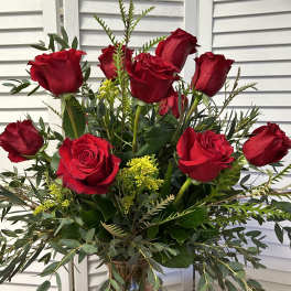Red roses arranged in a clear glass vase with greenery and yellow filler flowers