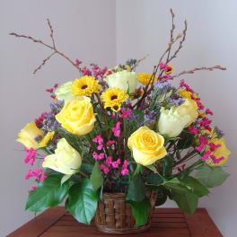 Yellow roses and daisies in a wicker basket with pink filler flowers