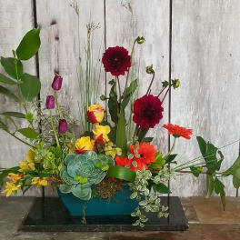 Mixed floral arrangement with red, orange, yellow, and purple blooms in a teal container
