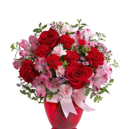 Red and pink flower arrangement in a red vase with a pink ribbon