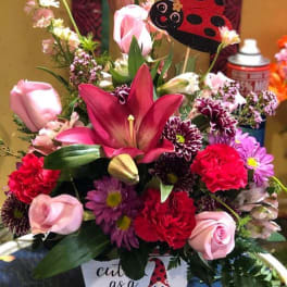 Mixed flower arrangement with a ladybug decoration in a white container