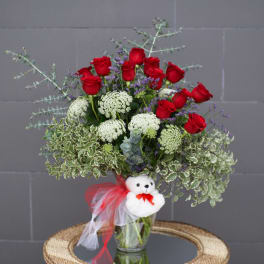 Bouquet of red roses with white filler flowers in a glass vase, decorated with a teddy bear