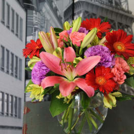 Mixed bouquet of pink lilies, red gerbera daisies and purple carnations in a clear glass vase