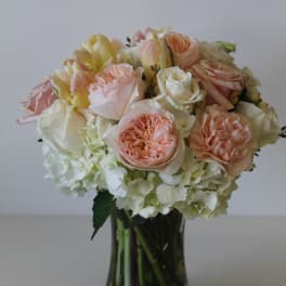 Round arrangement of peach and white roses and hydrangeas in a clear glass vase.