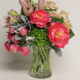 Pink peonies, tulips, lilies, and green hydrangea arranged in a clear glass vase