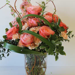 Tall arrangement of coral roses and peach carnations with looping greens in a clear glass vase