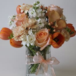Peach and white bouquet with roses, tulips, and calla lilies in a glass vase with ribbon