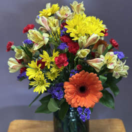 Mixed bouquet with orange gerbera, yellow daisies, and purple filler in a blue vase