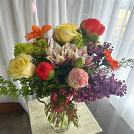 Mixed bouquet of roses, lilies, and purple blooms in a clear glass vase