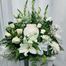 White floral funeral arrangement with roses, lilies, and a ceramic urn