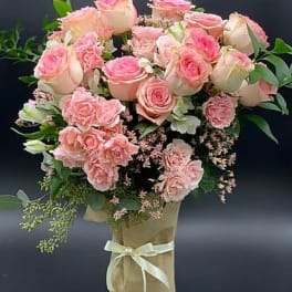 Pink roses and carnations arranged in a wrapped bouquet with a ribbon
