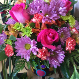 Bouquet of pink roses, purple daisies, and mixed blooms in a decorated vase
