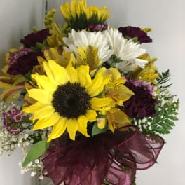 Bouquet of sunflowers, white daisies, and purple flowers with a burgundy ribbon