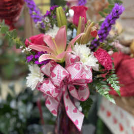 Pink lilies and roses with white daisies and a heart-patterned ribbon in a vase
