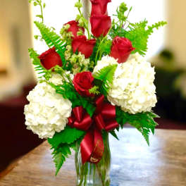 Red roses and white hydrangeas in a glass vase with a red ribbon