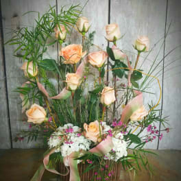 Tall arrangement of peach roses, white flowers, and pink ribbons