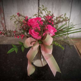 Pink roses in a clear vase with a large pale ribbon bow