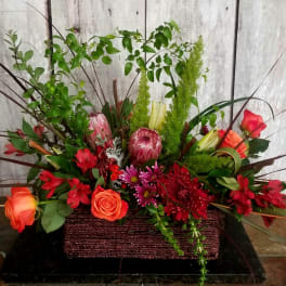 Mixed floral arrangement in a rectangular basket with red and orange blooms