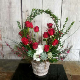 Red roses arranged in a white basket with succulents and greenery