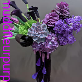 Purple floral arrangement with calla lilies, hydrangeas, and a succulent in a tall vase