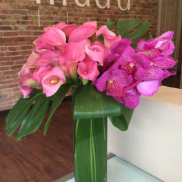 Pink calla lilies and purple orchids in a tall glass vase