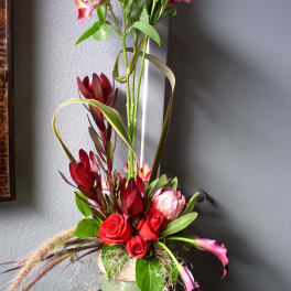 Tall floral arrangement with red roses and pink blooms in a green vase