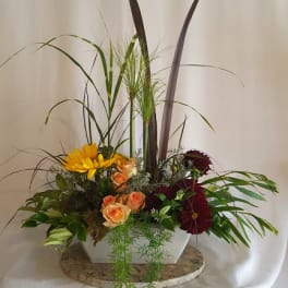 Mixed floral arrangement in a white rectangular vase with tall grass-like accents