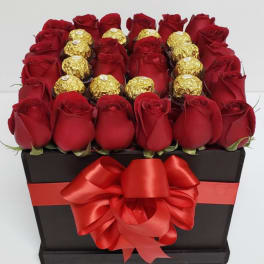 Red roses and gold-wrapped chocolates arranged in a black gift box with a red bow.